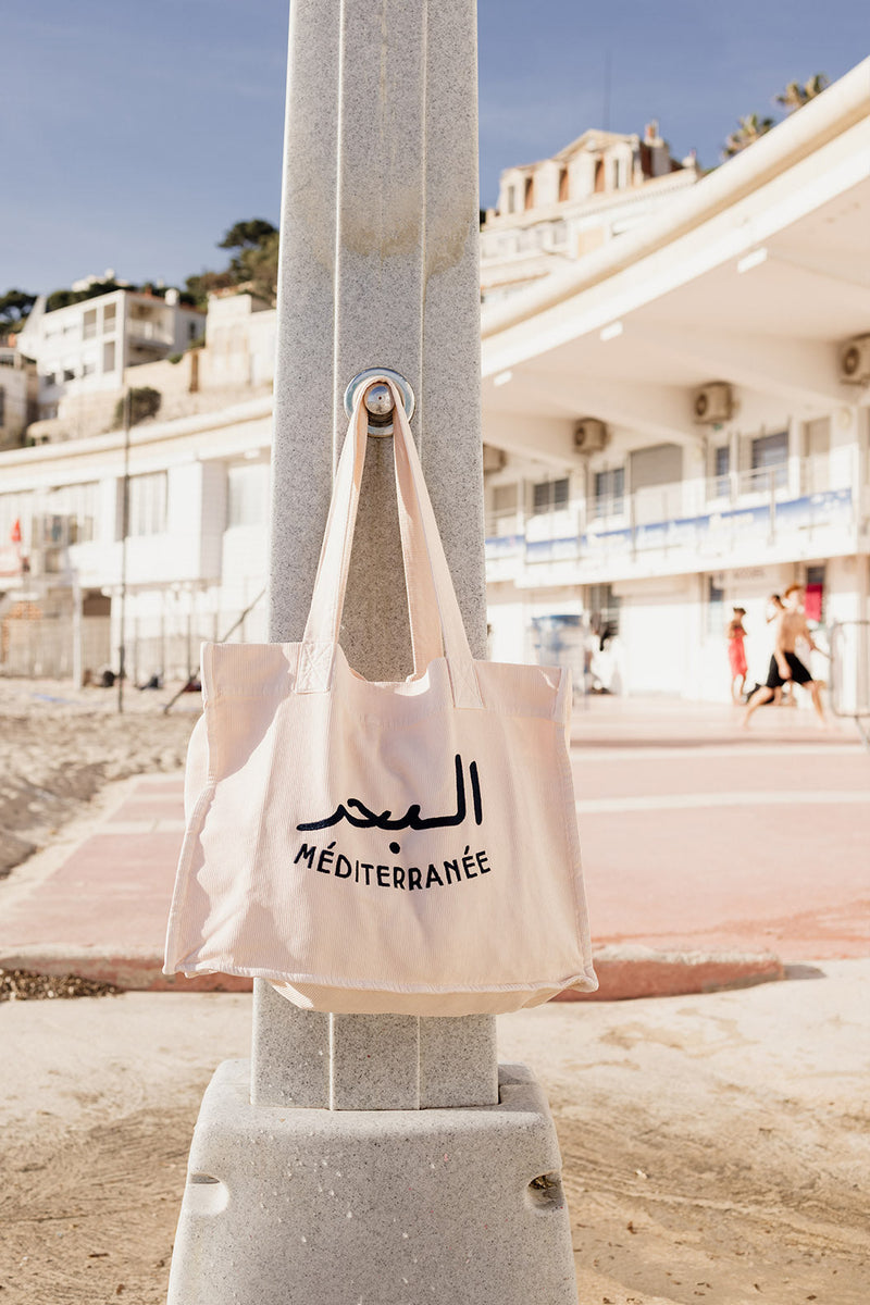 Sac cabas LYOUM accroché à une douche de plage.